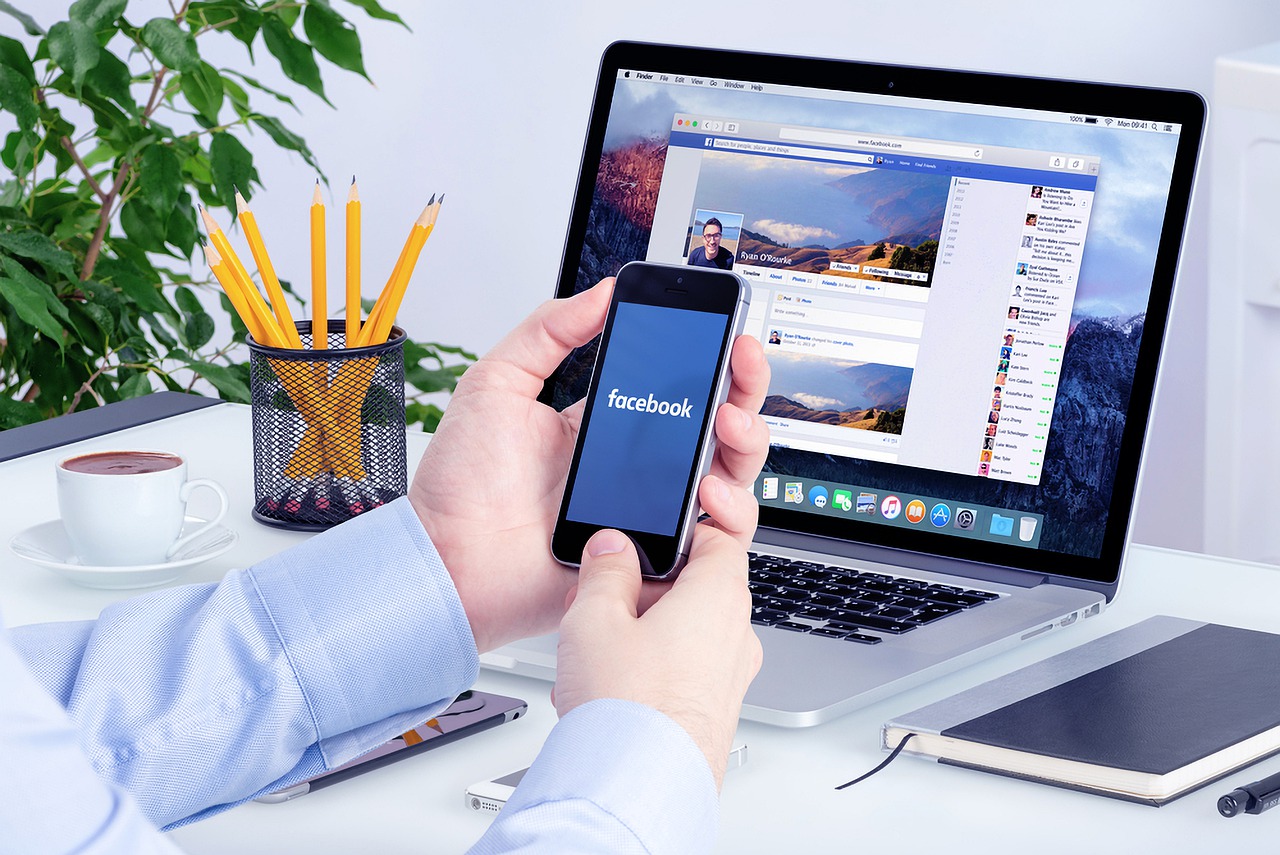 Seseorang sedang membuka aplikasi Facebook di laptop dan handphone untuk digital marketing